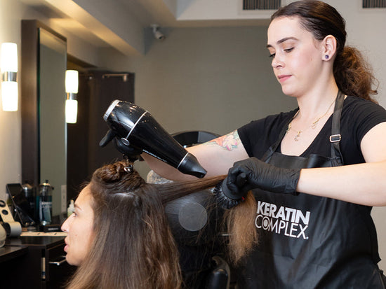 Hair stylist performing a blow-dry treatment using Keratin Complex products in a salon